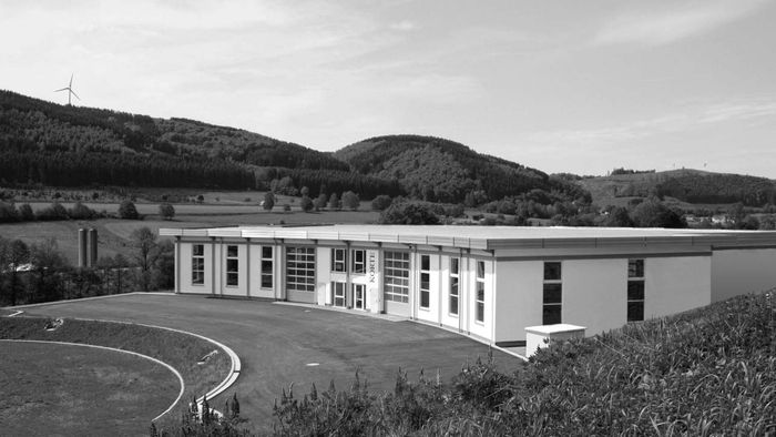 Schwarzweißaufnahme eines langgestreckten Betriebsgebäudes am Ortsrand von Plettenberg.