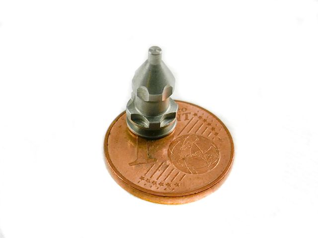 Ein wenige Millimeter großes, mehrstufig gefrästes Präzisionsbauteil steht auf einer 1-Cent-Münze.