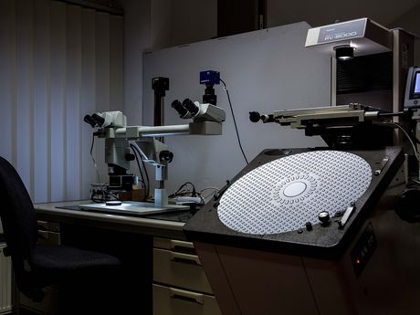 Messplatz mit Stereomikroskop, Profilprojektor und Messrechner an einer Werkbank.