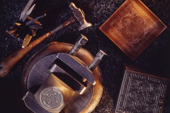 Graveurwerkzeuge, Stichel und Hammer neben handgravierten Messingplatten auf dunklem Stein.