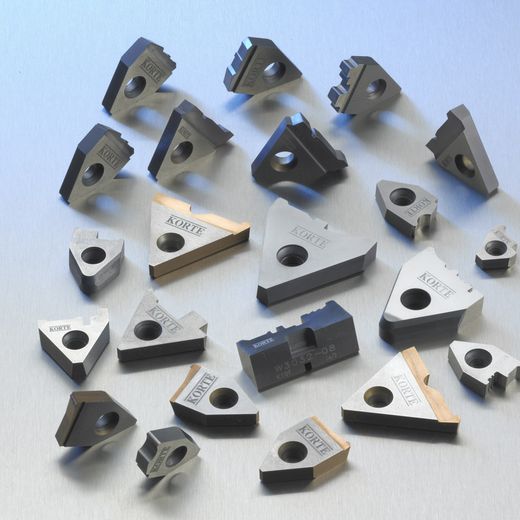 Verstreute Wendeschneidplatten und Formeinsätze aus Hartmetall in verschiedenen Geometrien.